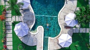A swimming pool with a unique guitar-shaped design, surrounded by green artificial grass and stone pathways. - Aldi's Bungalow and Homestay (Kuta)