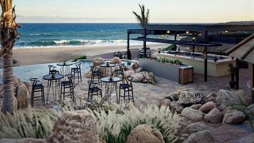 An outdoor seating area with tables and chairs, a pool, and a view of the ocean.