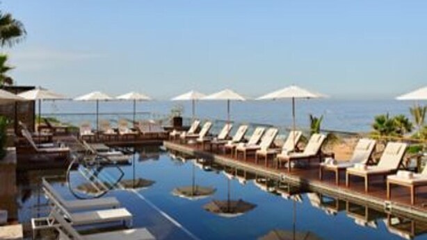 A poolside area with lounge chairs and umbrellas, a clear view of the ocean, and a dock with boats. - Zadun, a Ritz-carlton Reserve (San José del Cabo)