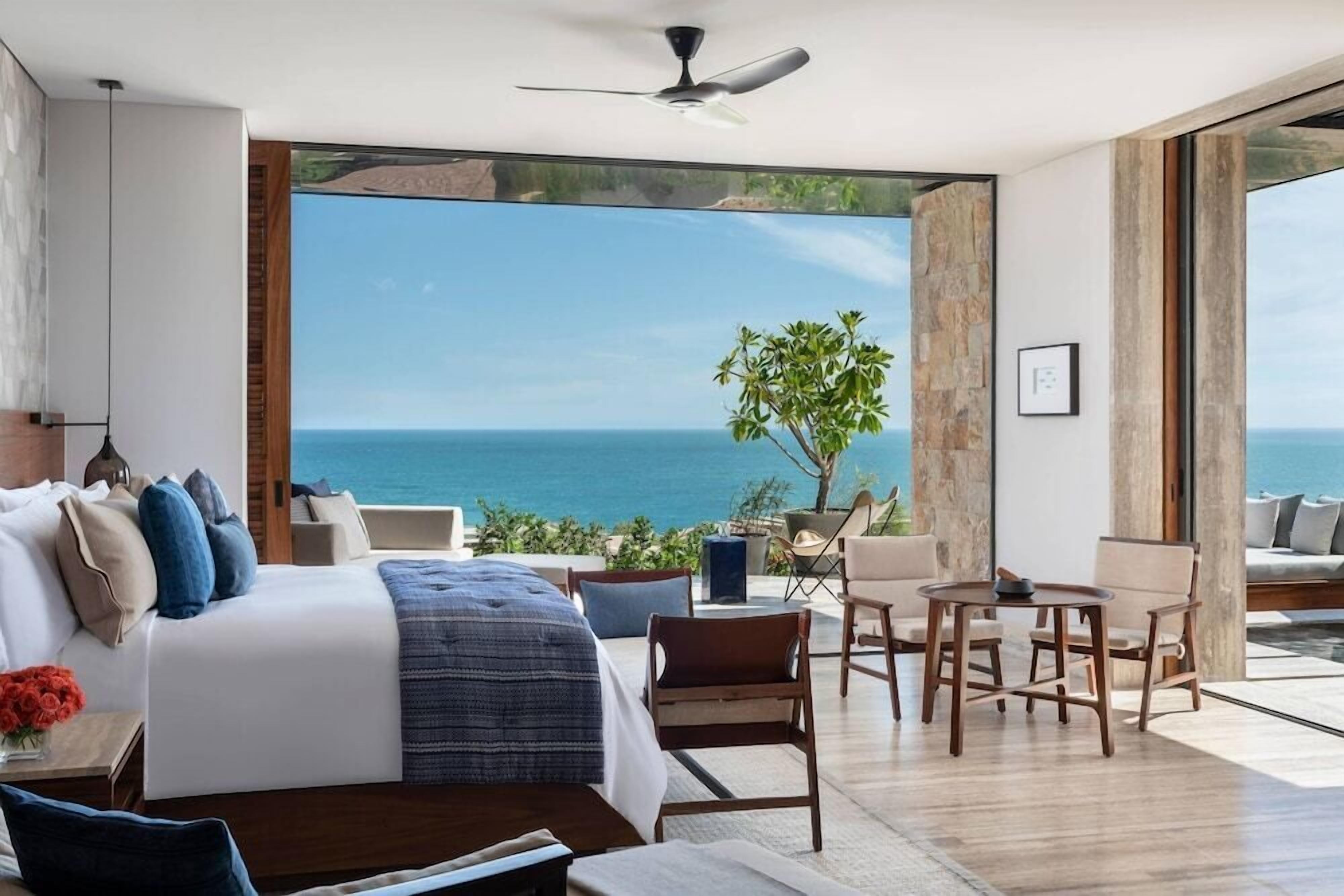 A bedroom with a large bed, a ceiling fan, and a view of the sea.