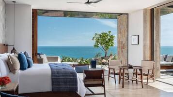 A bedroom with a large bed, a ceiling fan, and a view of the sea.