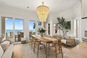 Ein geräumiger Essbereich mit Holztisch und -stühlen, einer Kristallleuchter und großen Fenstern mit Blick auf das Meer.
