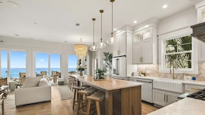 A modern kitchen with a large island, pendant lights, and a view of the ocean. - GULF-FRONT w/ Private Beach! Private Pool, Hot Tub! Sleeps 24! (Rosemary Beach)