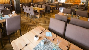 A restaurant with wooden walls and herringbone flooring, featuring tables and chairs arranged for dining. - Hotel Restaurant Löwen (Rust)