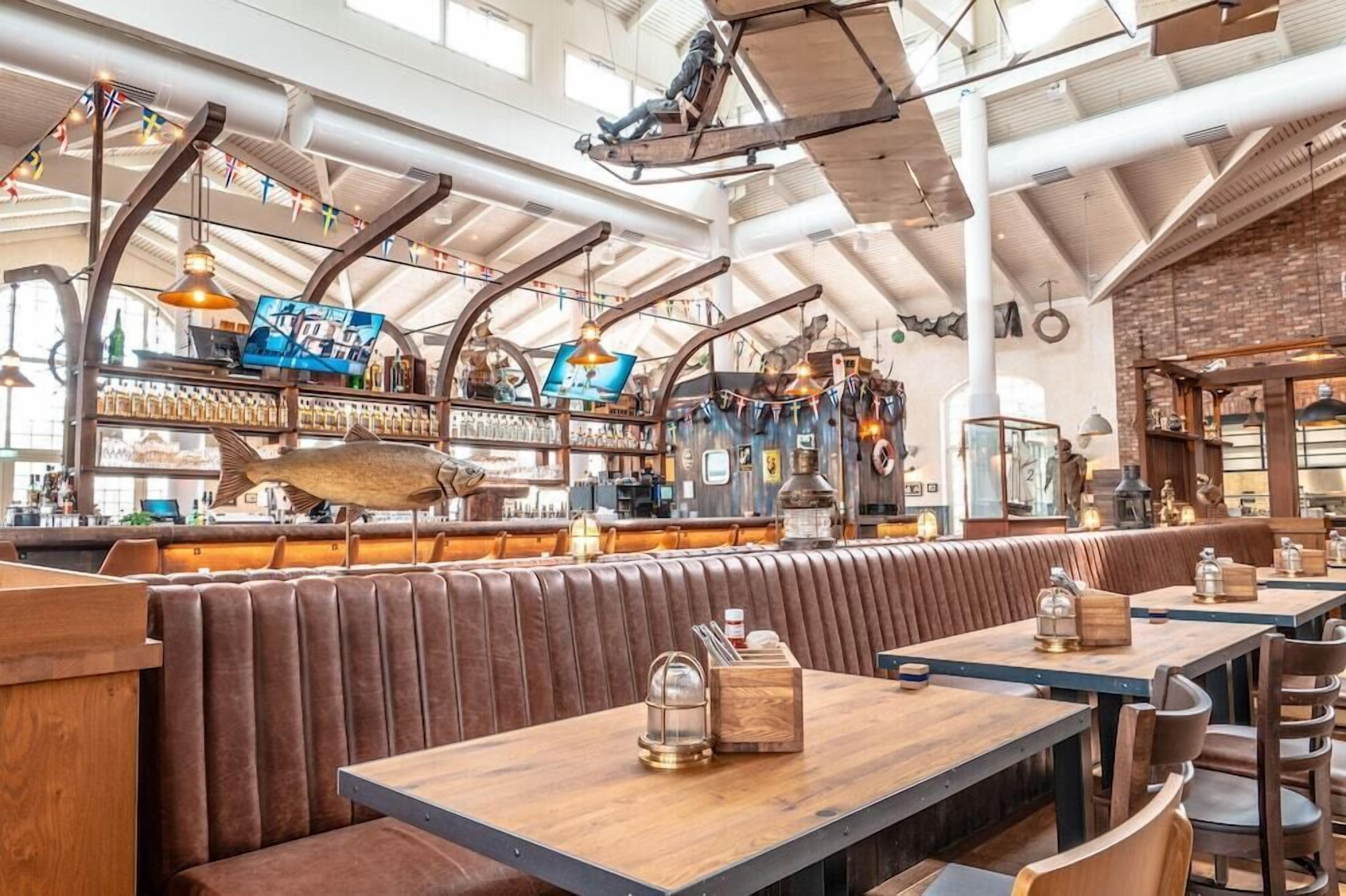 Un restaurant avec de hauts plafonds, des conduits apparents et un long comptoir avec des tabourets.