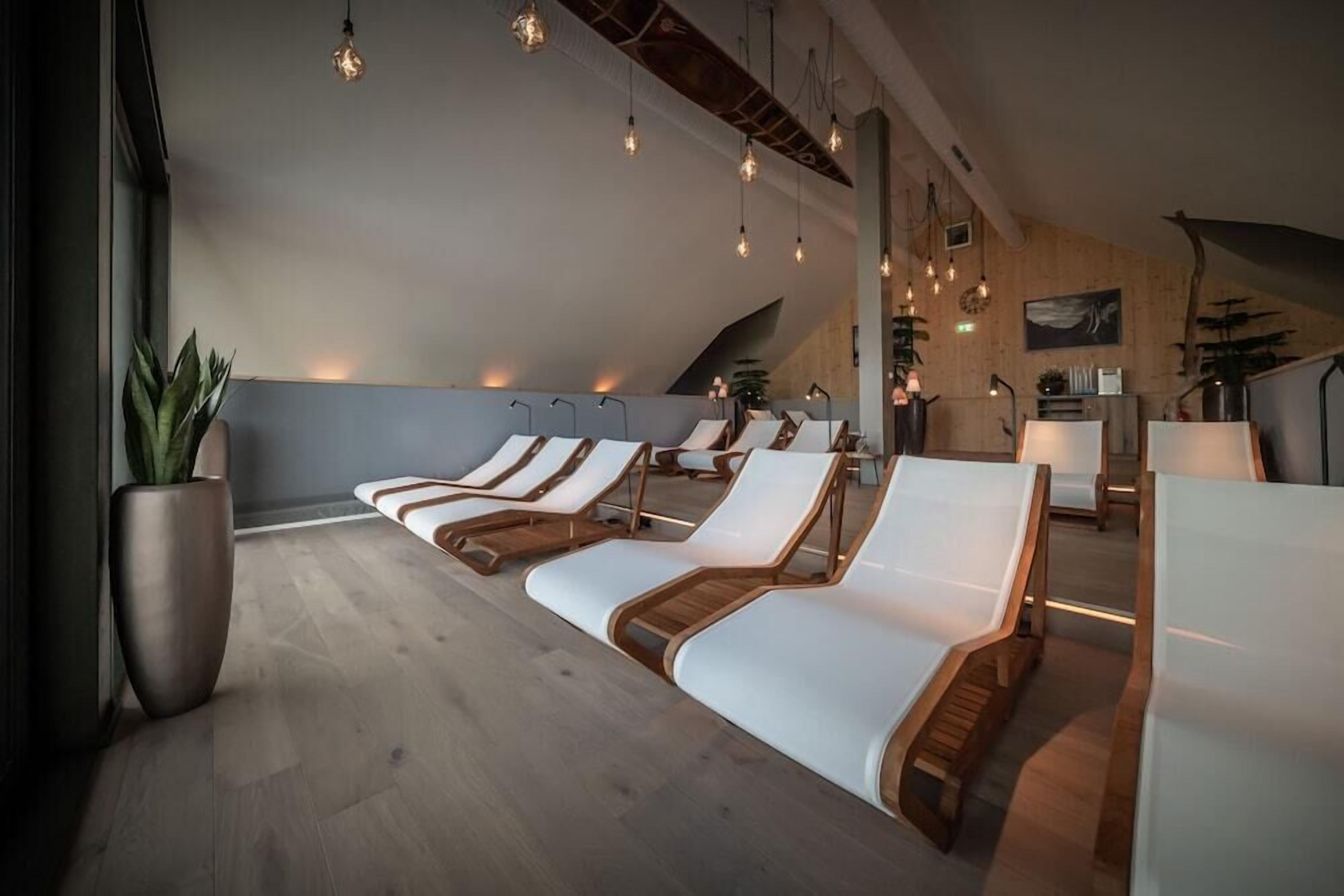 Un espace de détente moderne avec des chaises longues en bois, une grande plante en pot et un éclairage suspendu.