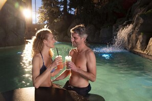 Two people sitting at a table by a pool with a waterfall feature in the background. - Europa Park Freizeitpark Erlebnis Resort Hotel Kronasar (Rust)