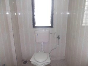 A small, tiled bathroom with a toilet, a window, and a sink. - Hotel Oasis (Daund)