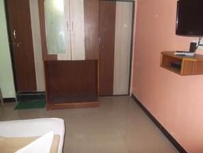 A hotel room with a bed, a wooden wardrobe, a television mounted on the wall, and a small wooden shelf with a remote control. - Hotel Oasis (Daund)