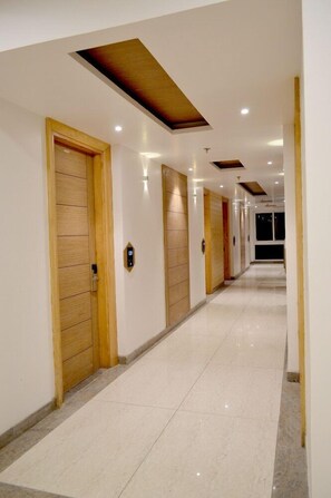 Un largo pasillo bien iluminado con puertas de madera y piso de baldosas.