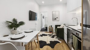 Une cuisine moderne avec des meubles blancs, un tapis en peau de vache noir et blanc, et un coin repas avec des chaises blanches et une table dressée pour deux personnes.