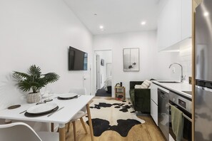 A modern kitchen with white cabinetry, a black and white cowhide rug, and a dining area with white chairs and a table set for two. - City Tree Hutt  -  A (Wellington)