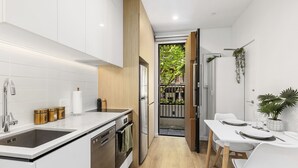 Une cuisine moderne avec des meubles blancs, des appareils en acier inoxydable et un coin repas comprenant une table et des chaises blanches.