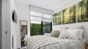 Une chambre moderne avec un grand lit, une porte-fenêtre coulissante donnant sur un balcon et trois œuvres d’art murales sur le thème de la forêt.