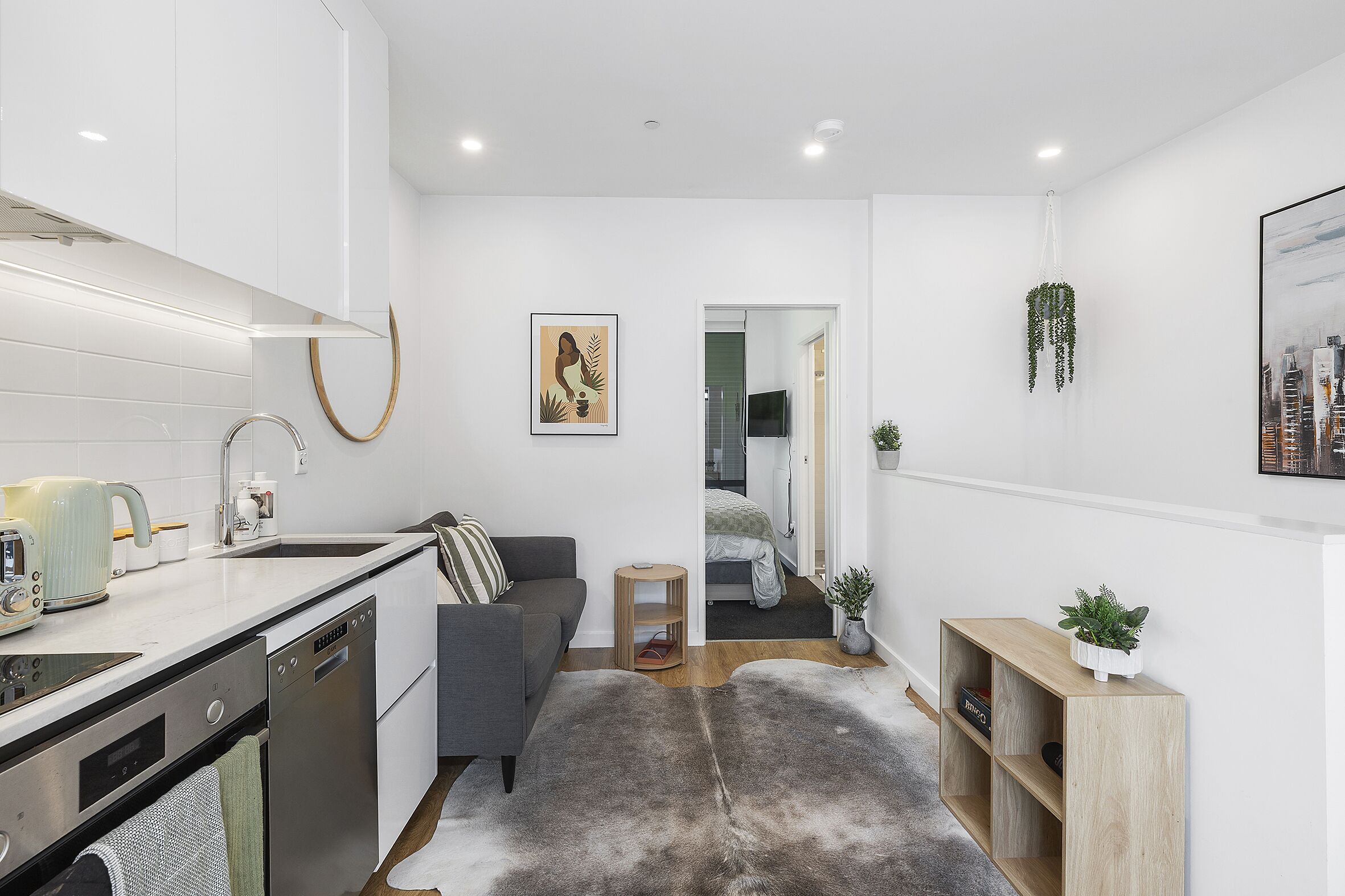 Una cocina moderna con armarios blancos, un sofá gris y un aparador de madera con plantas.
