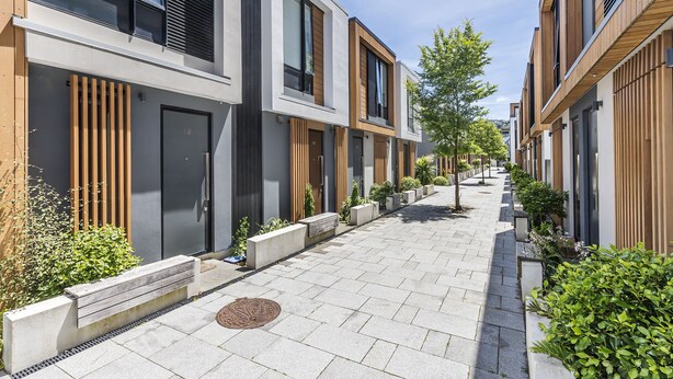 En modern bostadsgata med likadana hus, en tydlig gångväg och grönområden.