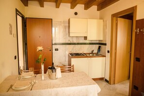 Cocina compacta con encimera de mármol, armarios de madera y comedor con mesa para dos.