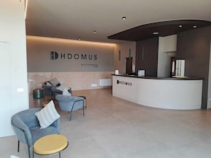 A modern reception area with a curved desk, two grey armchairs, and a small round table. - DA Franco (Nogarole Rocca)