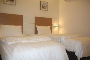 Une chambre d’hôtel avec deux lits, chacun doté de draps blancs et d’une tête de lit. Un luminaire mural est fixé sur le mur, du côté droit de la pièce.