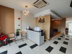 A hotel reception area with a check-in counter, two chairs, a potted plant, and a fire extinguisher. - Bangi Business Hotel (Bandar Baru Bangi)