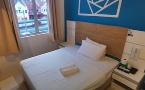 Une chambre d’hôtel avec un lit, une table de chevet, une fenêtre avec des rideaux et une vue sur les bâtiments environnants.