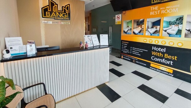 A hotel reception desk with a modern design, featuring a logo, a reception counter, and a large informational poster advertising room types and amenities. - Bangi Business Hotel (Bandar Baru Bangi)