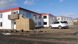 Een modern gebouw met een rood dak en witte muren, een houten omheining en een witte SUV die ervoor geparkeerd staat.