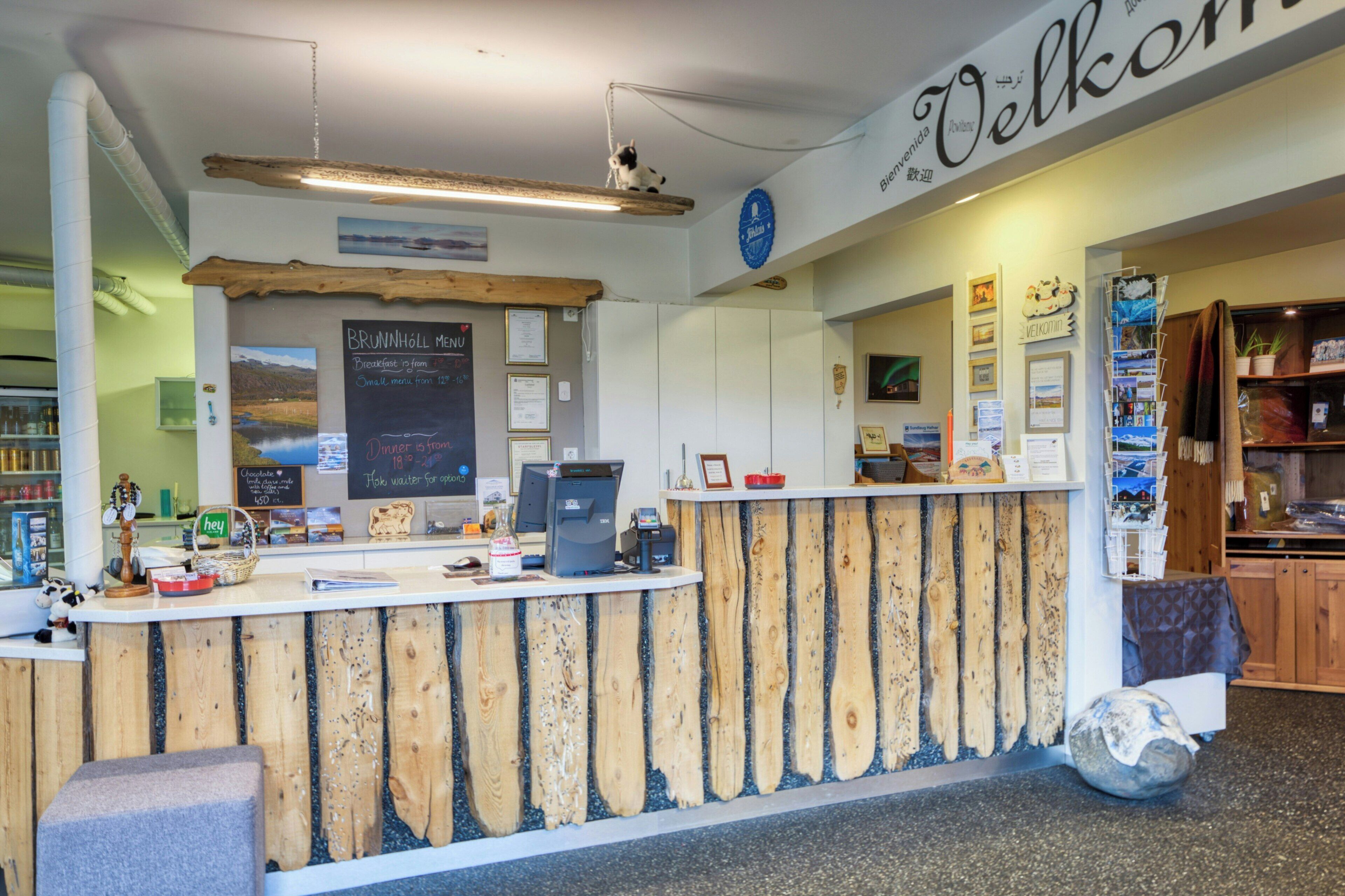 A reception desk with a wooden design, a 'Welcome' sign, a menu board, and a computer.