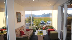 A cozy room with a sofa, a small table, and a view of a parking area with cars and mountains in the distance. - Brunnhóll Country Guesthouse (Höfn)