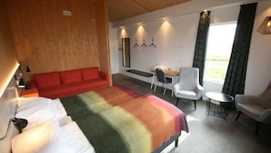 Een hotelkamer met een groot bed, een rode bank, een kleine tafel met stoelen, en uitzicht op het omliggende landschap door een raam.