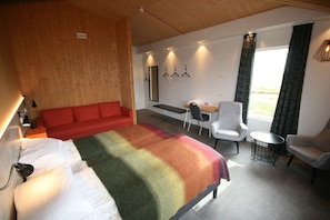 Et hotelværelse med en stor seng, en rød sofa, et lille bord med stole og udsigt til det fri gennem et vindue.