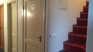 Un couloir avec trois portes, dont une porte sur laquelle est apposé un panneau indiquant les toilettes, et un escalier rouge à motifs.