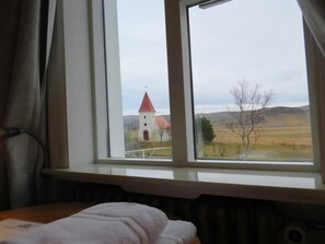 A room with a bed, a window with a view of a church and landscape. - Kalfafellsstadur Bed & Breakfast (Kalfatellsstadhur)