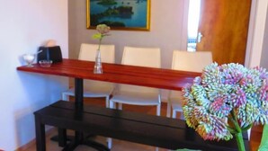 Un coin repas avec une table en bois, des chaises blanches, un vase de fleurs et un banc.