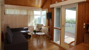 A cozy living room with a sofa, a small table, and a wicker chair. There is a sliding glass door leading to an outdoor deck. - Reynivellir (Reynivellir)