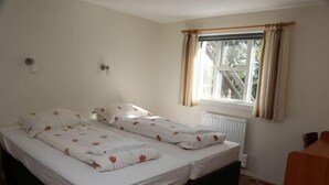 A double bed with white bedding and red floral patterns, a window with curtains, and a radiator. - Reynivellir (Reynivellir)