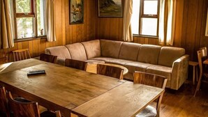 A cozy room with a wooden dining table, a beige sofa, and two windows with curtains. - Reynivellir (Reynivellir)