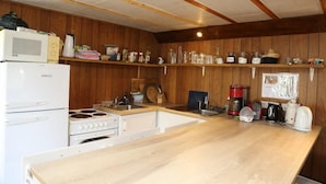 A compact kitchen with wooden paneling, a white refrigerator, a stove, a sink, and various kitchen utensils and appliances. - Reynivellir (Reynivellir)