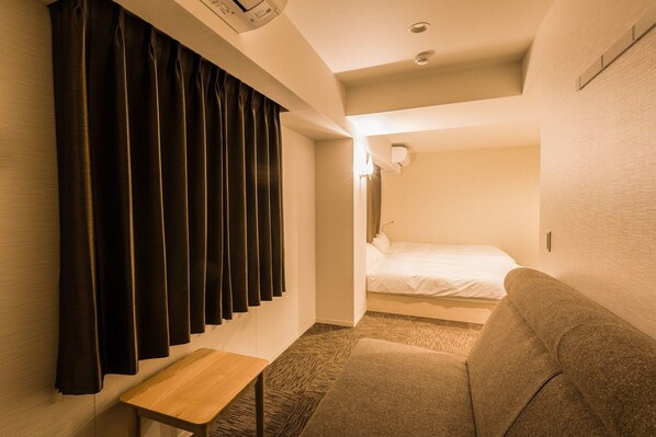 A narrow hallway with a bench, a bed, and a wall-mounted air conditioning unit. - Hotel Ninestates Hakata (Fukuoka)