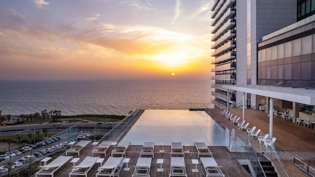 A rooftop pool with lounge chairs and a view of the sunset over the ocean. - West Lagoone Hotel (Netanya)