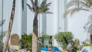 A pool area with palm trees, lounge chairs, and a white building with arches. - Palm Djerba (Mezraia)