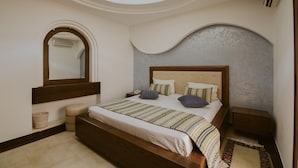 A bedroom with a skylight, a large bed with multiple pillows, a bedside table, and a small stool. - Palm Djerba (Mezraia)