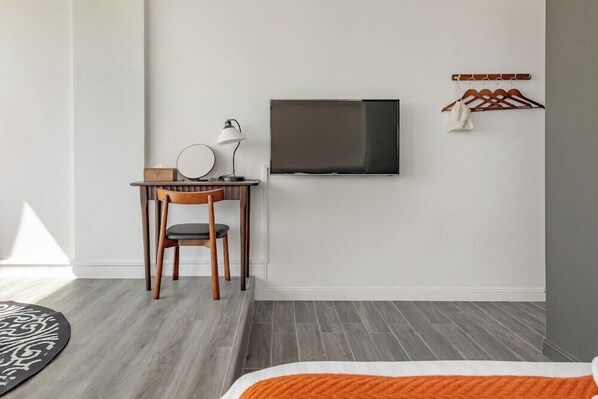 A modern hotel room with a bed, a desk with a chair, a television mounted on the wall, and a coat rack with hangers. - Nan Fang B&B (Liuqiu)