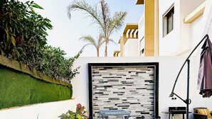 A modern outdoor patio with a metal table, a decorative wall, and various plants.