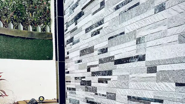 A modern bathroom with a black sink and a white circular basin, a tiled wall with a geometric pattern, and a window with a view of greenery.