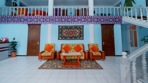 Eine großzügige Lobby mit hoher Decke, einem zentralen Sitzbereich mit gemusterten Sofas, einem dekorativen Teppich und einer Treppe mit Geländer.