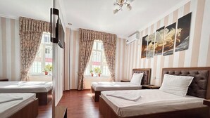 Ein Hotelzimmer mit zwei Einzelbetten, einem größeren Doppelbett, Holzböden, gestreifter Tapete und einem Gemälde an der Wand.