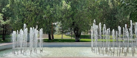 Una fuente con múltiples chorros de agua rodeada de árboles y un borde de baldosas.