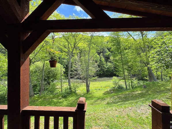 A wooden gazebo with a view of a lush green forest and a river.