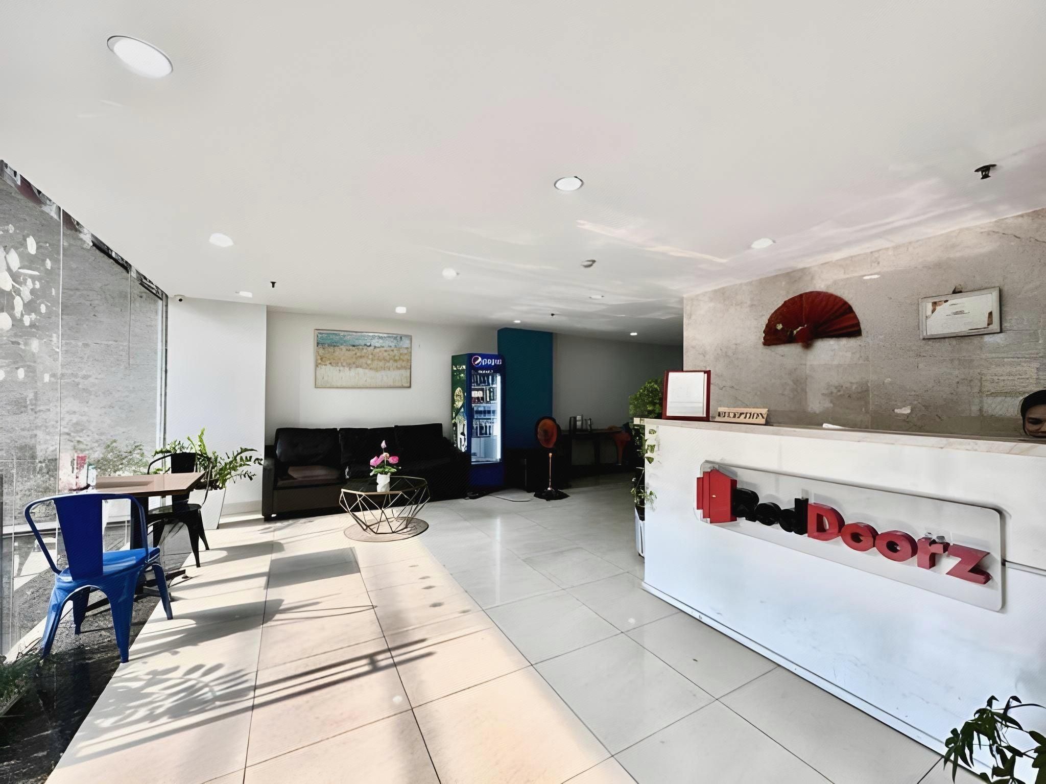 A reception area with a white reception desk, a blue chair, a sofa, and a potted plant.